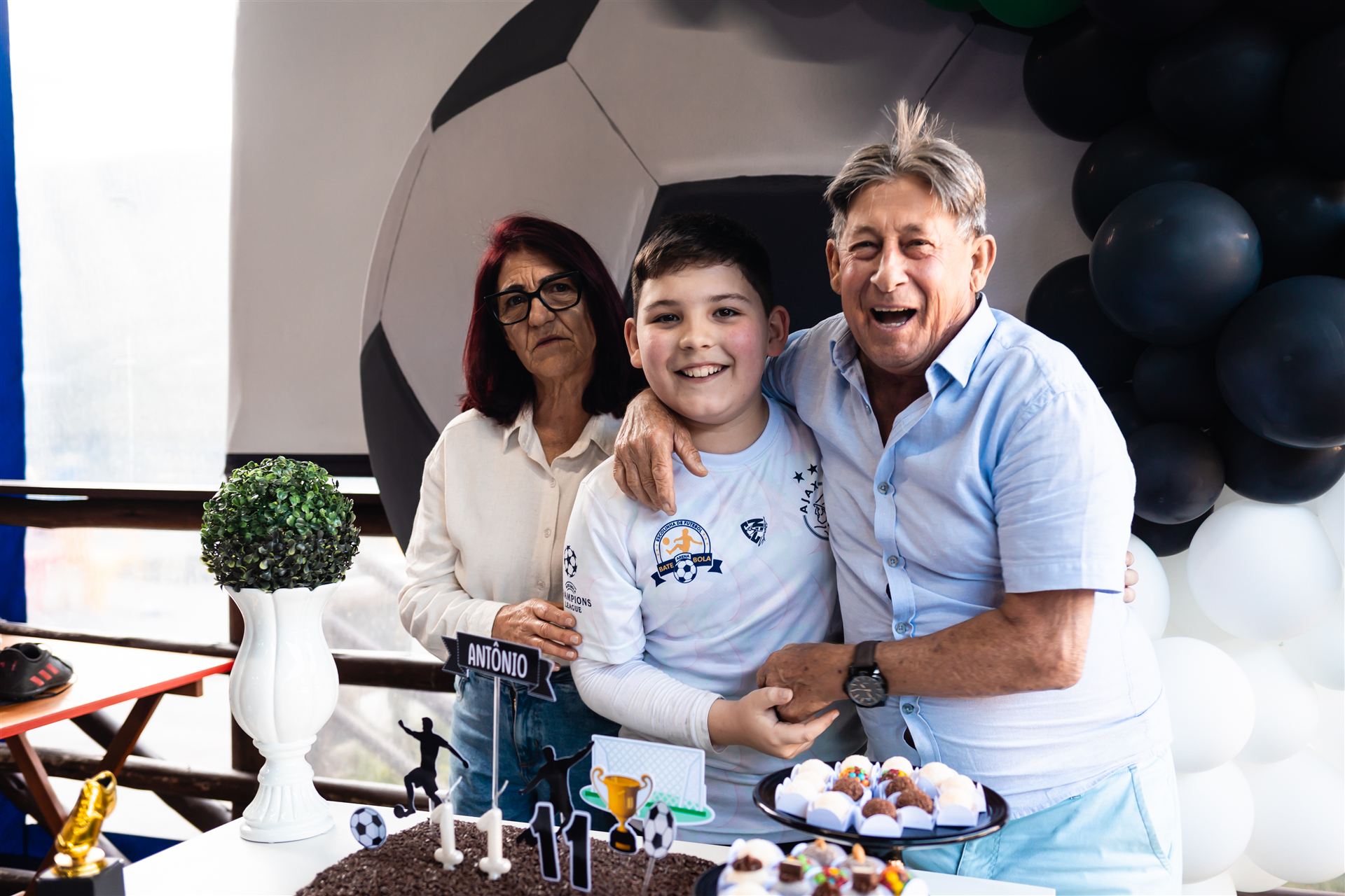 Criança comemorando aniversário temático de futebol com avós no salão Maria da Festa